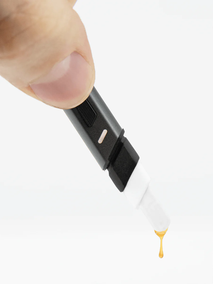 A hand is holding a black and white electronic device, which appears to be a pen or stylus, and there is a drop of liquid coming out of it.