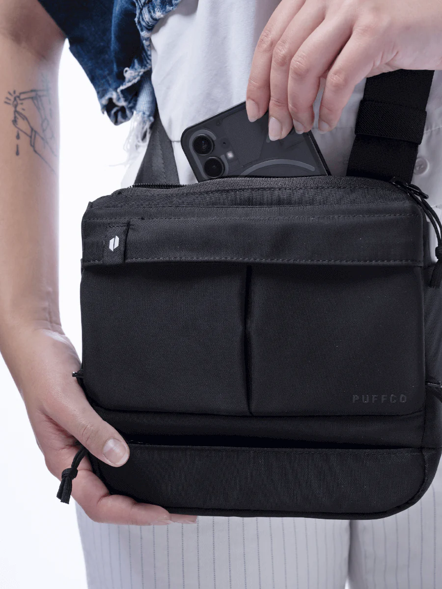 A person is holding a black bag with a Puffco logo, and they are reaching into the bag to take out a smartphone.