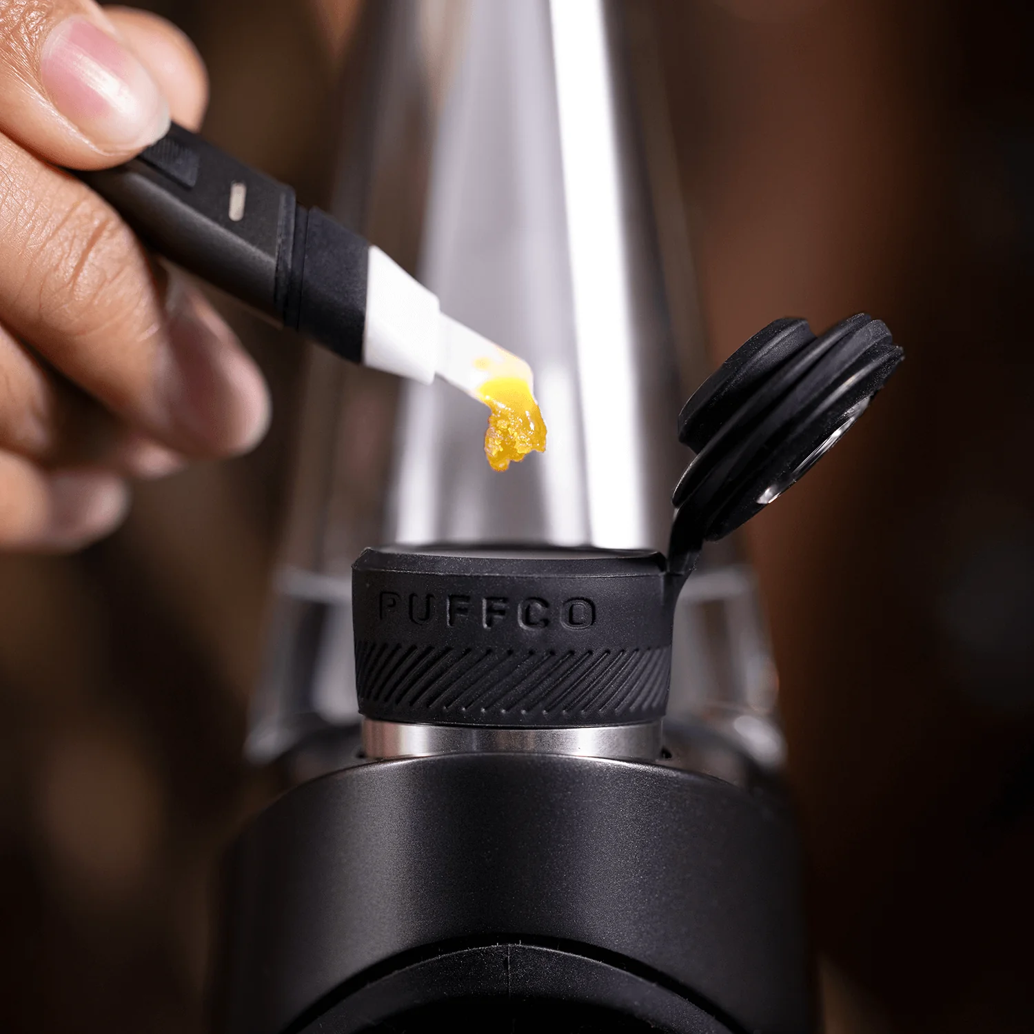 A hand is applying a yellow substance to a black cap with the word "PUFFCO" printed on it.
