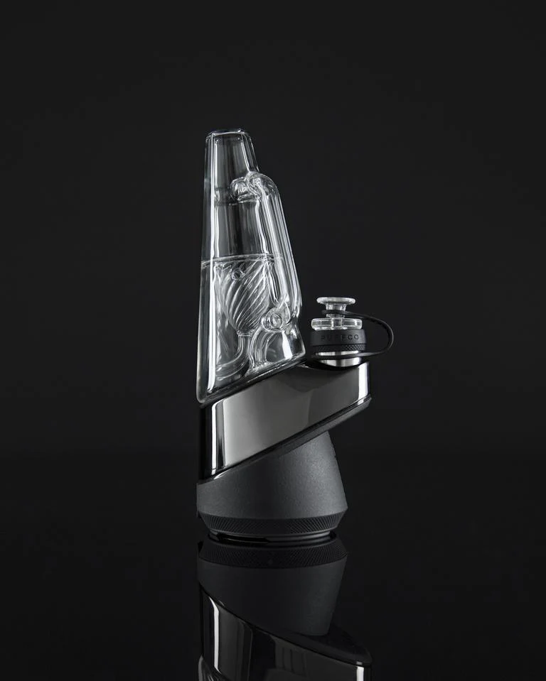 A sleek, modern-looking electronic device with a clear glass component, likely a piece of electronic equipment or a gaming accessory, set against a dark background.