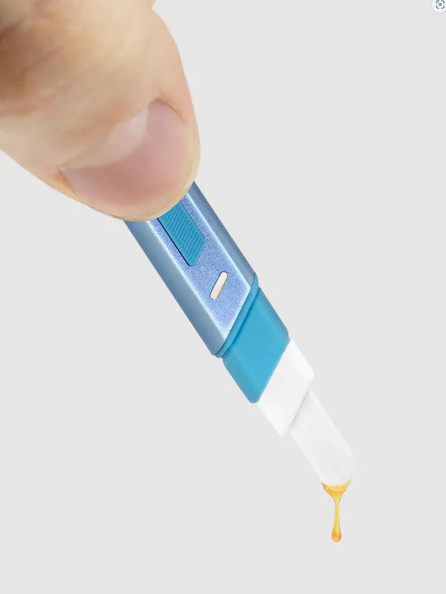 A blue and white electronic device, possibly a pen or stylus, is being held by a hand, with a drop of liquid, possibly ink, being released from the tip of the device.