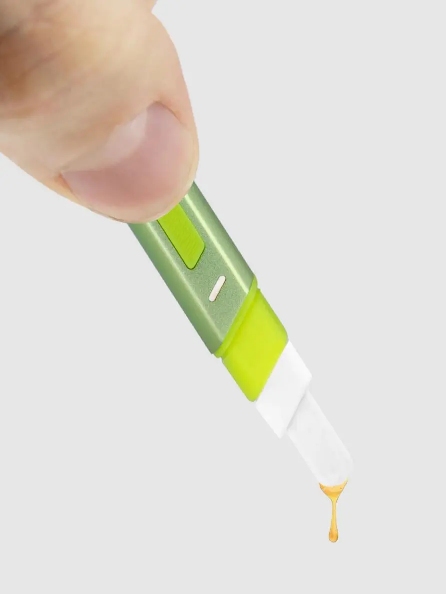 A hand is holding a green and white object, which appears to be a small, pointed tool with a yellow substance dripping from it.
