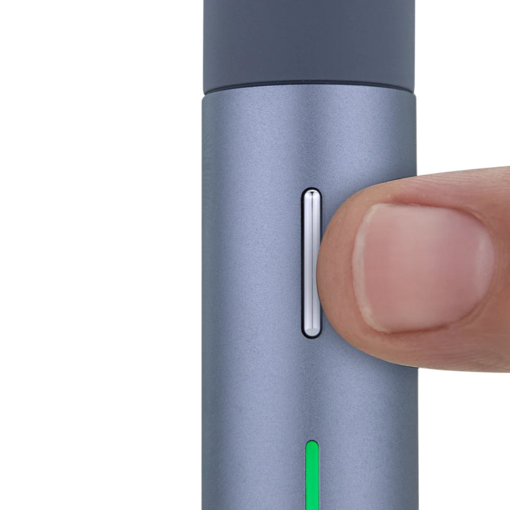 A close-up view of a thumb pressing a button on a gray object, which appears to be a small electronic device.