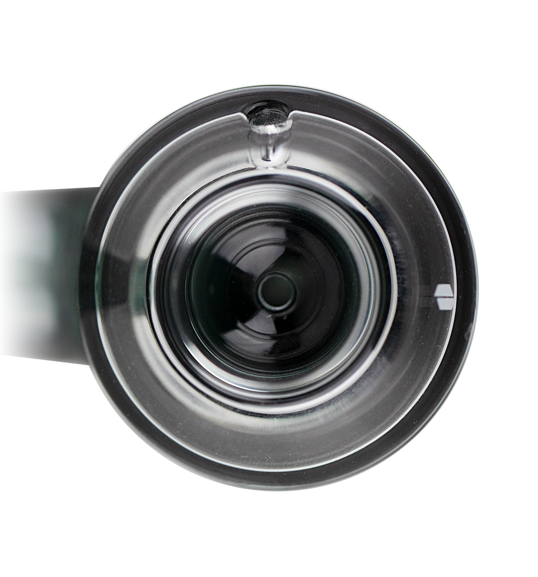 A clear glass container with a black lid, containing a small amount of green substance, is shown against a black background.