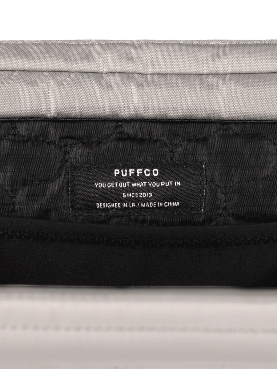 a close-up view of a black and gray bag, with a label on it that reads "PUFFCO YOU GET OUT WHAT YOU PUT IN SINCE 2013 DESIGNED IN LA / MADE IN CHINA".