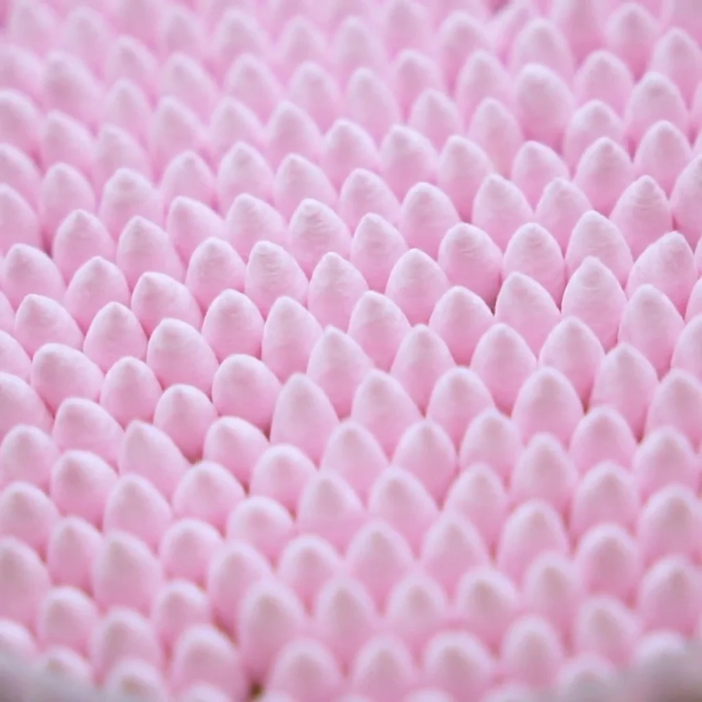 A close-up image of numerous pink cotton swabs arranged in a repeating pattern.