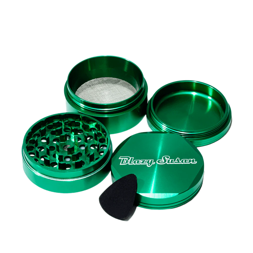 A set of green metal grinders and a black plastic pick, with the grinders open and the pick resting on top of the lid.