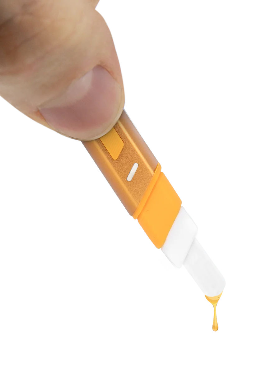 A close-up view of a person's finger holding a small, yellow object that appears to be a pen or marker, with a drop of yellow ink visible on the tip.