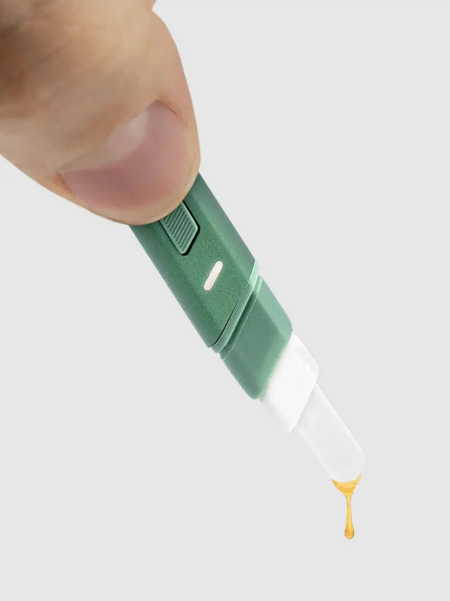 A green electronic device with a white tip is being used to drip a yellow liquid, possibly oil or honey, into a container.
